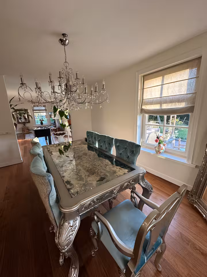 Dining room with a long table, upholstered chairs, a crystal chandelier and garden view