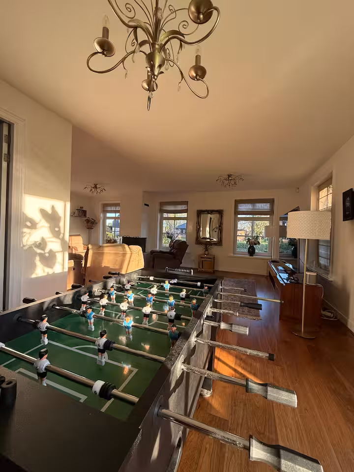 Foosball table in a bright room with wooden floors and the living area behind